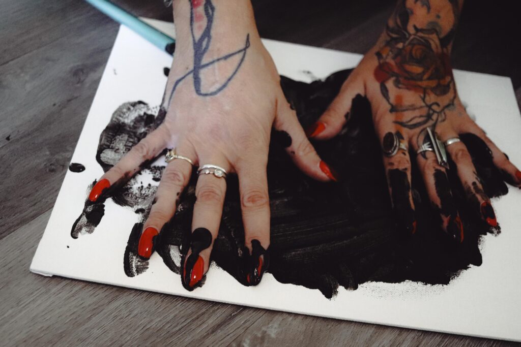 Hands with rings and long red nails smearing black paint on a piece of paper